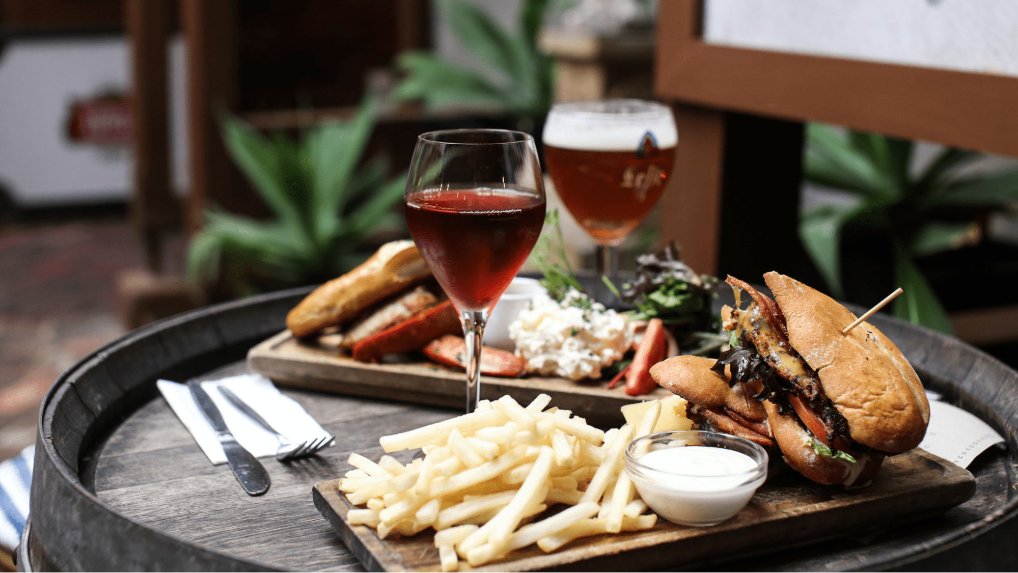 Glass of red wine next to a cheese burger and fries